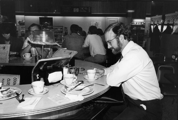 Steven O. Kimbrough enjoys a second cup of coffee at the lunch counter at the Rennebohm Drug Store No. 4 restaurant in the Hilldale Shopping Center, 702 N. Midvale Blvd. As a member of the University Board of Regents, former governor Oscar Rennebohm, the founder of the Rennebohm chain of drug stores, was active in the development of the University property as a shopping center.