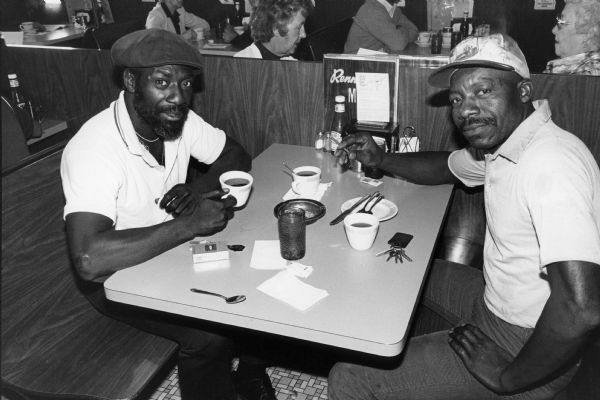 Two men enjoy coffee and a cigarette at an unidentified Rennebohm Drug Store restaurant. At this time cigarette smoking in Madison restaurants took place in restricted areas. Other diners can be seen behind their booth.