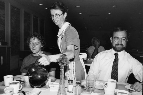 A waitress pours coffee at the Rennebohm Drug Store No. 6 restaurant in the First Wisconsin Bank on the Capitol Square. Steven O. Kimbrough is seated on the right. He and photographer Chuck Patch were engaged in a personal project to eat breakfast in and photograph all of the existing Rennebohms.