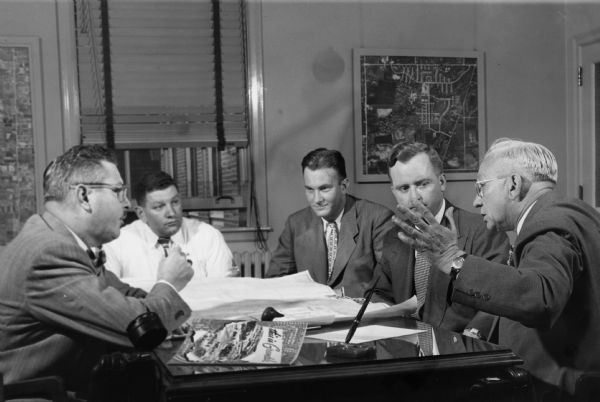 Governor Oscar Rennebohm, on the right, gesturing for emphasis, while meeting with a small group. Rennebohm, the founder and CEO of Rennebohm Drug Stores, Inc., did not begin his career until his nomination as lieutenant governor. During the 1940s he was one of a number of Wisconsin businessmen elected to high office without previous political experience.