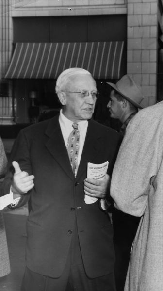 Oscar Rennebohm distributing Republican Party campaign literature during the 1956 campaign, probably in the Milwaukee area.  The brochure he is holding urges "Keep Wisconsin Strong."  The former governor, who was also the founder of the Rennebohm Drug Store chain, left office in January 1951.