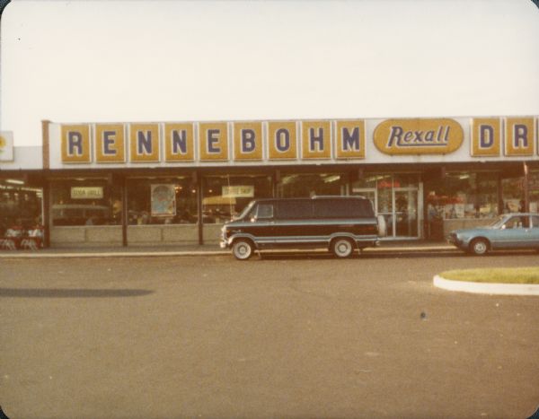 Color snapshot taken by amateur photographer Steven O. Kimbrough of an unidentified Rennebohm Drug Store with a car and a van parked in front. Kimbrough and friend Steve Patch were engaged in a project to eat breakfast in all Rennebohms then in existence.