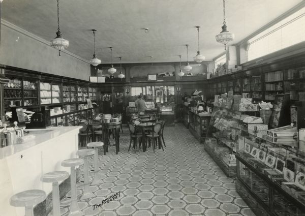 Interior views of the new Rennebohm Drug Store #1, 1357 University Avenue at the corner of Randall Avenue, including the soda fountain and tables on the left, art deco light fixtures, pharmacy at the rear, and the cigar counter on the right.