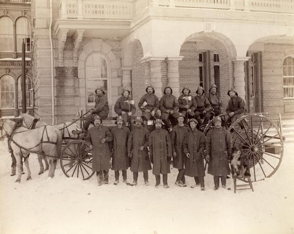 Group portrait of the Northern Hospital for the Insane's institutional fire fighting department posed outside the building. Horse-drawn transport cart and hose equipment and the departmental dog are included in the view.