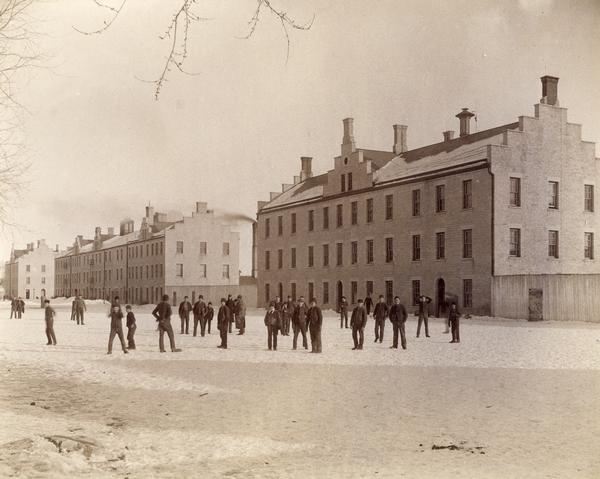 Students gather in the schoolyard at the Wisconsin Industrial School for Boys. Several school buildings are seen in the background.