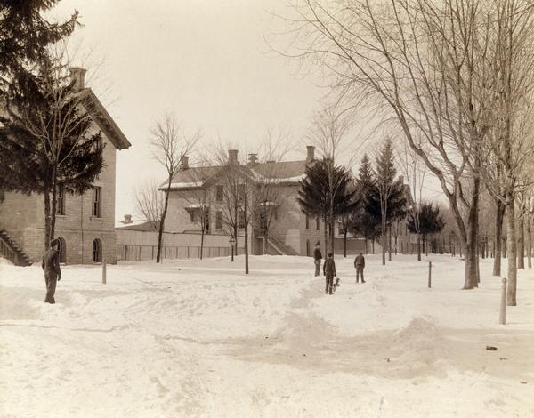 Winter scene with four students from the Wisconsin Industrial School for Boys standing outside on the snow-covered school grounds.