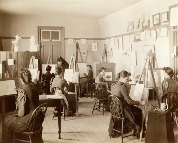 Female students practice painting and drawing in an art class session at the State School for the Deaf as a teacher assists in the background.