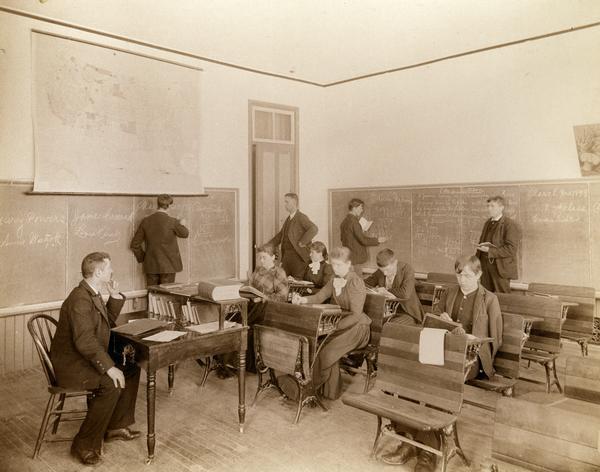 Male and female students read and practice math at the State School for the Deaf as a teacher looks on from the head of the class.