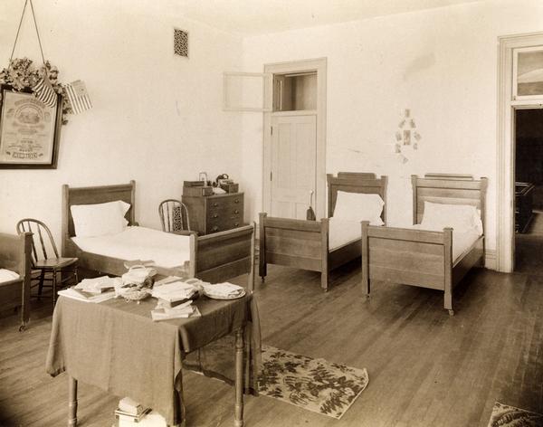 Sleeping quarters at the State School for the Blind, with four single beds, a dresser, a chair, and a table.