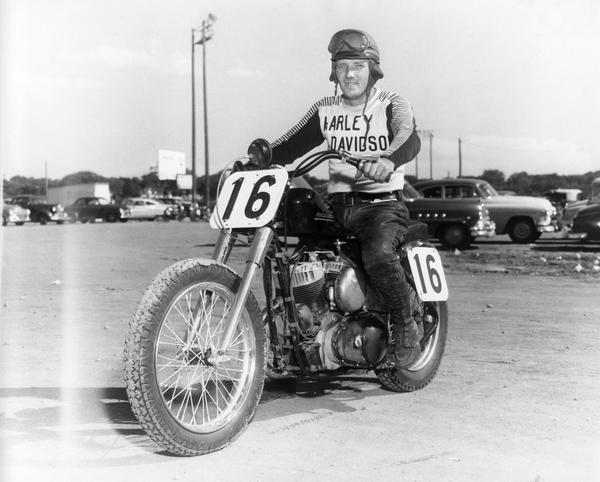 Jimmy Chan of Columbus, Ohio, expert motorcycle racer, sits astride his motorcycle, No. 16, wearing a Harley Davidson jersey and racing gear at Wisconsin State Fair Park.