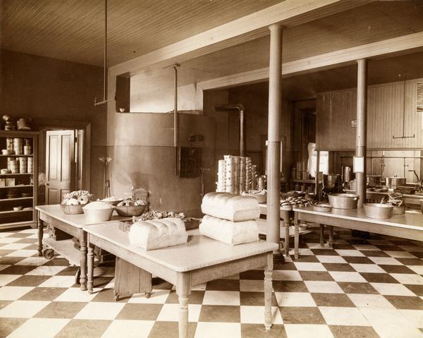 Freshly-baked loaves of bread are stacked on tables with bowls and trays of other food items in the large kitchen at the Wisconsin State Hospital for the Insane (Mendota Mental Health Institute).