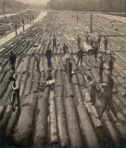 Group of lumber workers standing on logs floating in Beef Slough.