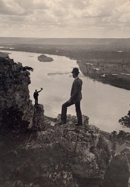 Two men posing on bluffs overlooking the Mississippi River at Fountain City. Fountain Brewery is visible at bottom right.