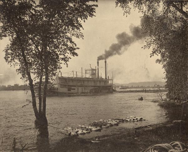 View from shoreline of the sternwheel steamer "E. Rutledge," owned by Weyerhaeuser & Denkmann's Rock Island Lumber Company, picking up a raft of logs at Beef Slough, for transport to its sawmill downstream.