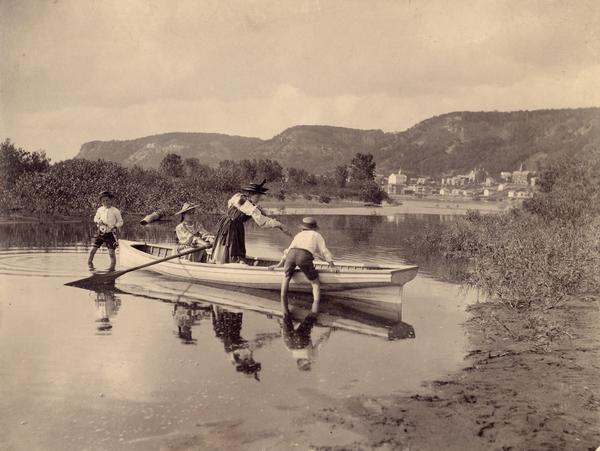 Group of children playing in a rowboat in a Mississippi River inlet. Alma, Wisconsin is in the background on the opposite shoreline.