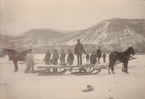 Several men and a horse-drawn sled harvesting Mississippi River ice. Alma, Wisconsin is visible in the background.