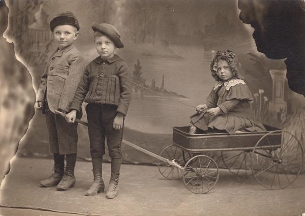 Studio portrait of Gesell children. Two boys, Arnold in center, pulling girl in wagon.