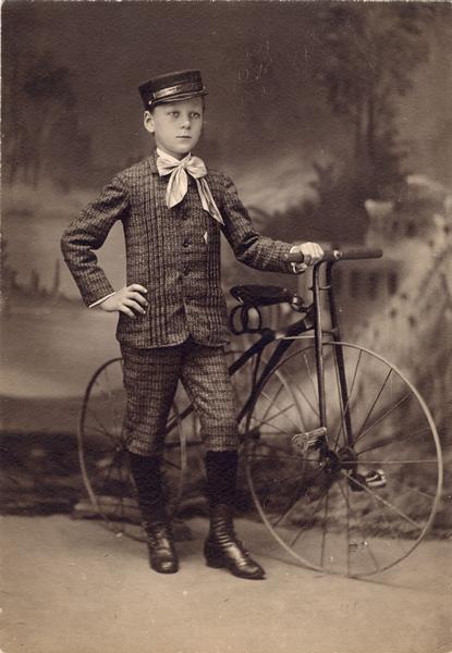 Full-length studio portrait in front of a painted backdrop of Arnold Gesell with a large tricycle.