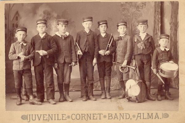 Studio portrait in front of a painted backdrop of Juvenile Coronet Band of Alma, Wisconsin, with boy holding instruments. Arnold Gesell is third from right.

