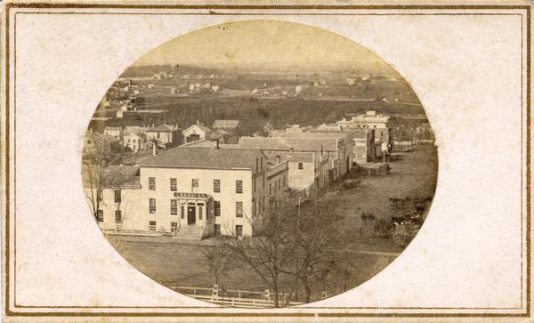 North Pinckney Street and East Washington Avenue from the Capitol roof. The American House, which burned down in 1868, is one of the businesses shown in this view. Several residences are also in the image.
