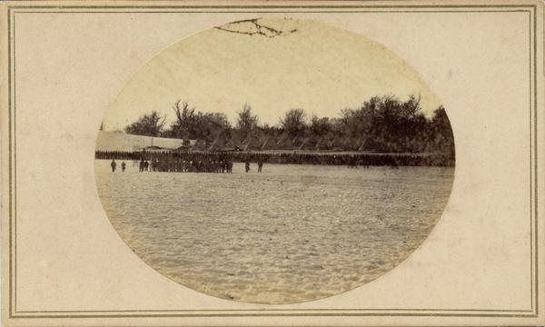 Soldiers in formation at Camp Randall during winter. The season [there appears to be snow on the ground] and the tents indicate that this image was made in 1861 or 1862. Improved quarters for the soldiers were erected in 1862. The camp was used as a training ground for most of Wisconsin's Civil War soldiers. This image was probably taken near the corner of University Avenue and Randall Street.