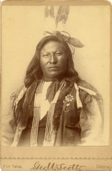 Waist-up studio portrait of Rain in the Face, member of the Sioux Nation, in traditional costume.