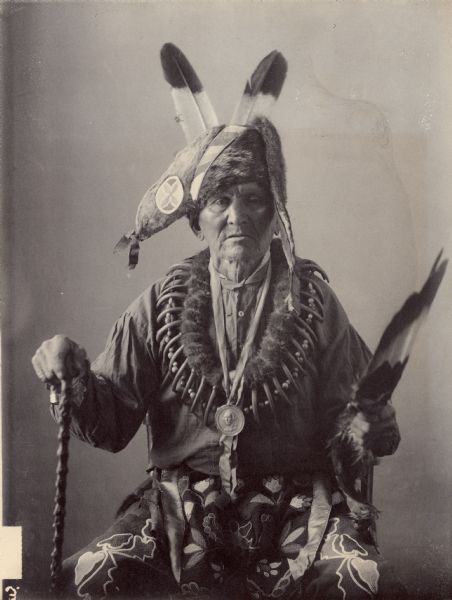 Studio portrait of Ahblocoenazin (Standing On the Prairie), called John Grant (Mixed Blood), with Peace Medal, Headdress and Bear Claw Necklace. Part of the Siouan (Sioux), Iowa, Dakota Tribes.
