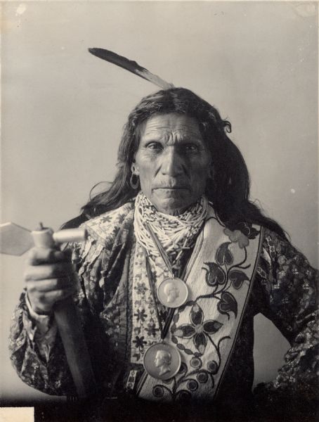 Studio portrait of Oto man, (George) Arkeketah, Head Chief. Part of Siouan (Sioux) and Otoe Tribes. He wears two medals and holds an axe.