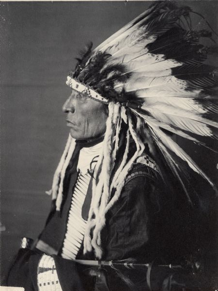 Profile studio portrait of Candi Tanka or Big Tabbaco, with headdress, and holding possibly a pipe. Part of Siouan (Sioux) and Yankton Tribes