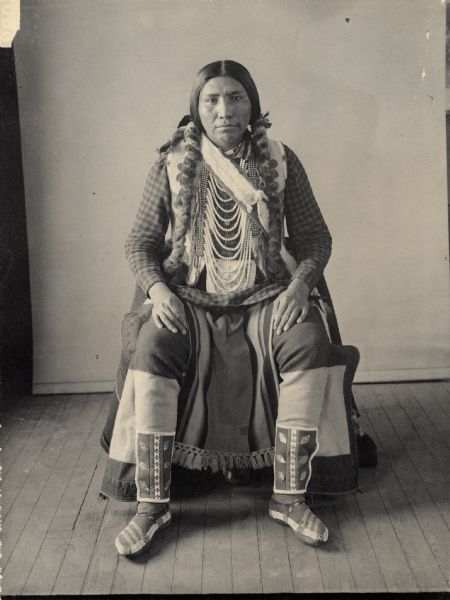 Studio portrait of George Caperty in partial native dress with ornaments and beaded bag. Part of Shahaptian and Yakima Tribes