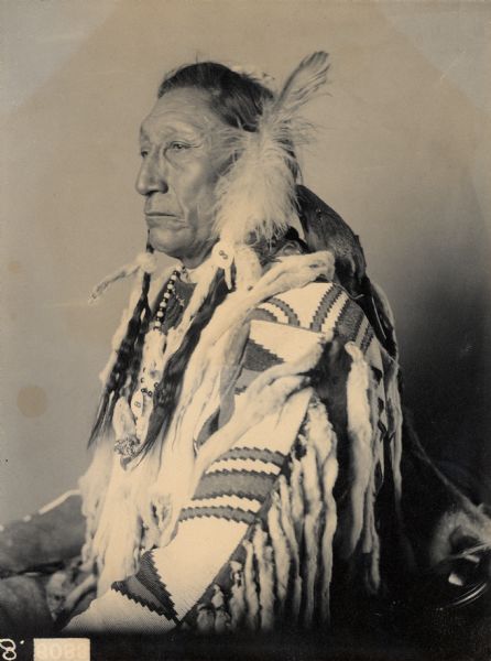 Studio portrait of Car-Io-Scuse (Curly Bear) in native dress with ornaments. Part of the Siouan (Sioux) and Blackfoot Tribes.