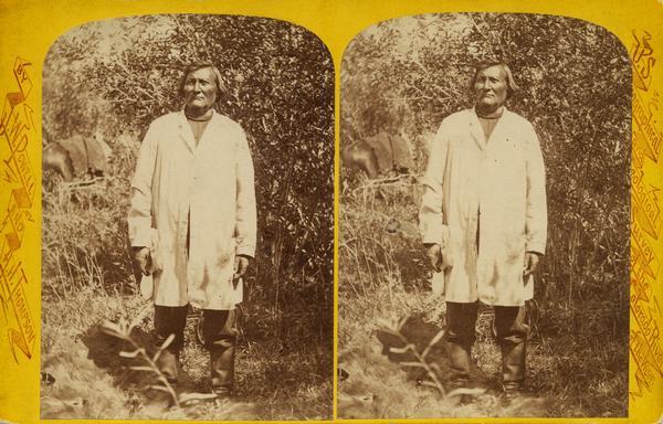 Stereograph of Ta-vah-puts, Chief of the U-in-tah Utes, standing in a field.