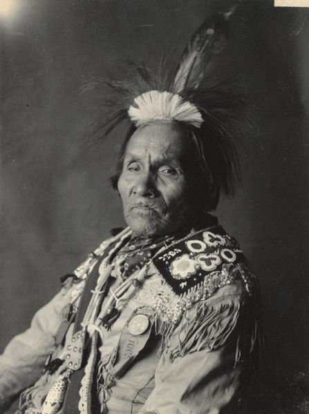 Portrait (Profile) of Hodjiage-De (Fish Carrier) or (He Bears A Fish by The Forehead Strap), called William Henry Fishcarrier, in native dress with headdress and ornaments and holding pipe- tomahawk. Part of Iroquian and Cayuga Tribes.