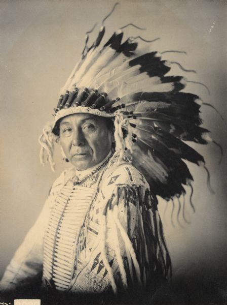 Portrait of Maka Zi (Yellow Earth), called John Lone-Dog, in native dress with headdress and breastplate. Part of Siouan (Sioux) and Yankton Tribes.