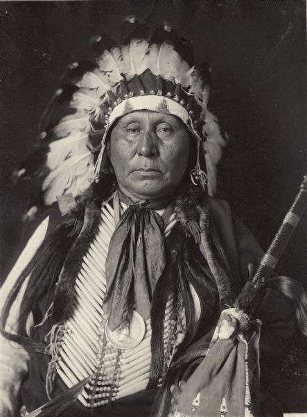 Portrait (Front) of Mi-Xa-Ton-Ga (Big Goose) in partial native dress with headdress and breastplate and peace medal and holding pipe? Part of Siouan (Sioux) and Ponca Tribes.  