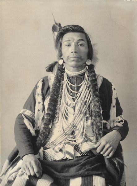 Studio portrait of Bill Owhie, son of Head Chief, in native dress with ornaments. Part of Shahaptian and Yakima Tribes.