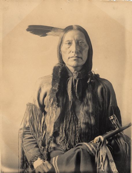 Portrait (Front) of Scabby Bull or Black Crow in native dress and holding pipe. Part of Algonquian and Arapaho Tribes.
