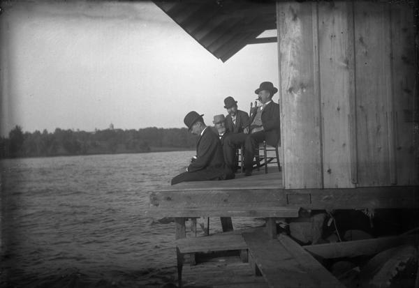 Four men sit on the balcony of Rocky Roost, the vacation home designed by Frank Lloyd Wright. Located west of Governor's Island in Lake Mendota. The men are (left to right) A.B. Morris, W.A.P. Morris, A.J. Dodge, and Melville C. Clark.