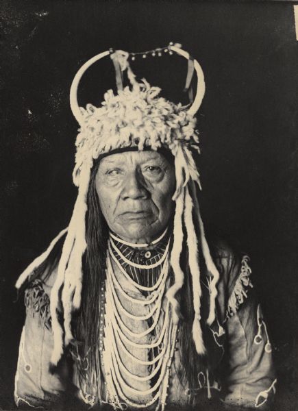 Studio portrait of Chief Slum-Xi-Ki (Bear Claw), Called Charlot, in native dress with horned headdress and ornaments. Part of Salishan and Flathead Tribes.