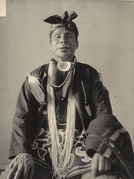 Studio portrait of Bashicta-Nogueb (High Up In The Sky), called Charles Sucker, in partial native dress with ornaments. Part of Algonquian and Chippewa Tribes.