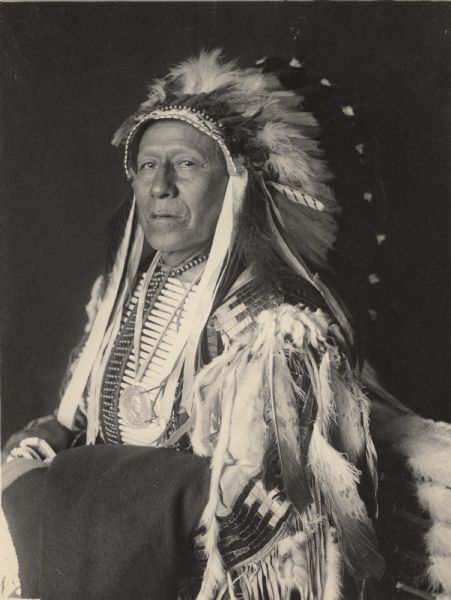 Studio portrait of Chief of Loafer Band, Ta-Semke-Tokeco, Called Paul Strange Horse, in native dress with headdress, ornaments and peace medal. Part of Siouan (Sioux) and Brule Tribes.
