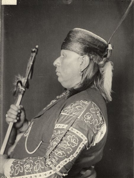 Profile studio portrait of Wa-Shin-Ha (Fat On Skin) odress with headdress and ornaments and holding possibly a pipe. Part of Siouan (Sioux) and Osage Tribes.