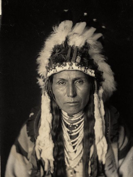 Studio portrait of Chief Albert Waters, successor to Chief Joseph, in native dress with headdress and ornaments. Part of Shahaptian and Nez-Perce Tribes.
