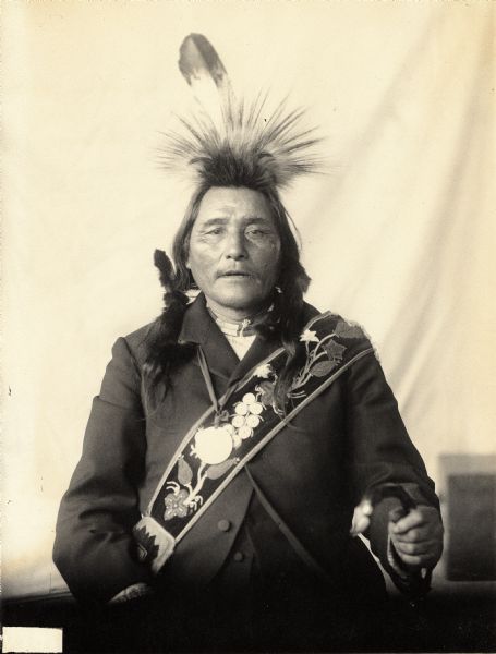 Studio portrait (Front) of Midriff or Diaphragm in partial native dress with peace medal, headdress and ornaments. Part of Algonquian and Chippewa Tribes.