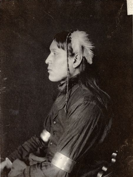 Profile studio portrait of Amos White-Swan in partial native dress. Part of Siouan (Sioux) and Brule Tribes.
