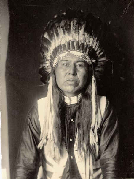 Studio portrait of Yumyekalimpt, called Jesse Stevens, Interpreter for Ahlakat, in partial native dress with headdress and ornaments. Part of Shahaptian and Nez-Perce Tribes.