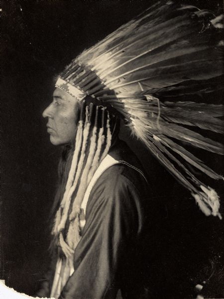 Profile studio portrait of Yumyekalimpt, called Jesse Stevens, Interpreter For Ahlakat, in partial native dress with headdress. Part of Shahaptian and Nez-Perce Tribes.