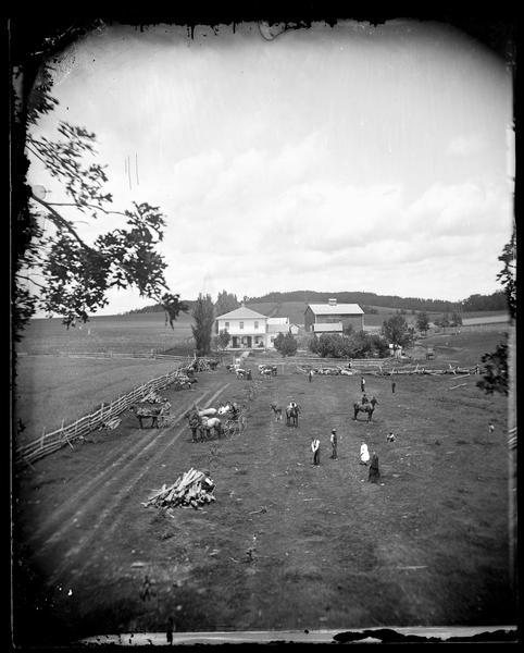 People are playing croquet in a field in the foreground with other people, horses, cattle and carriages also posing in the field.  In the background, people are standing on the porch of a farmhouse, with outbuildings and a barn behind the house.