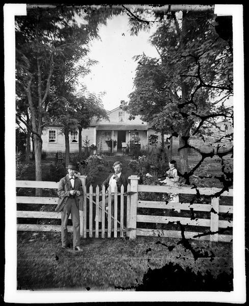 Halvor Skavlem (middle?), Gunil Olmstead Skavlem and a friend standing near the fence in front of Skavlem's frame home, with an unidentified man reading on the porch. Halvor Skavlem later became sheriff of Rock County and was a prominent naturalist and archaeologist.