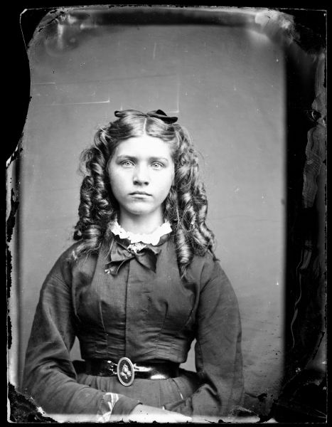 Waist-up portrait of girl with ringlets, and a belt at her waist with an ornate clasp.